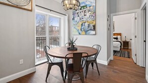 Un coin repas avec une table ronde, des chaises, un lustre et un grand tableau accroché au mur.