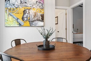 Una mesa de comedor con sillas, un jarrón con follaje y un cuadro de un caballo y una rueda de carruaje en la pared.