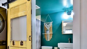 Et badeværelse med en turkis væg, et hvidt toilet, en hvid vask og et gulv med et sort-hvidt mønster.