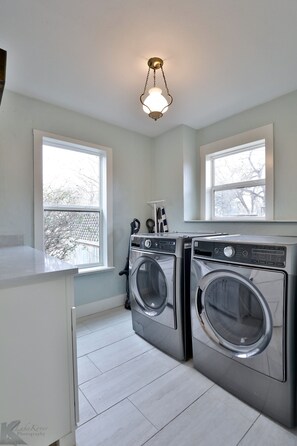 A laundry room with two front-loading washing machines, a white countertop, and a hanging rack with clothes.