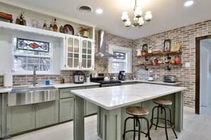 A kitchen with a large island, stainless steel appliances, and a brick wall.
