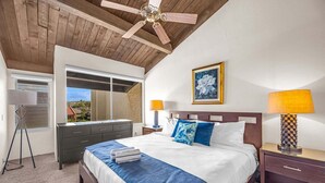 A bedroom with a bed, a ceiling fan, a dresser, a nightstand, a lamp, and a framed picture on the wall. - Cozy Beachside Retreat Steps from Kamaole III (Kihei)