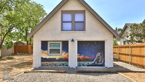 Una casa con techo a dos aguas, un pequeño porche delantero y un mural en el lateral.