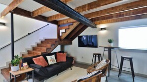Una sala de estar moderna con un sofá negro, una escalera de madera y un televisor de pantalla plana montado en la pared.