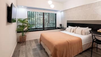 Un dormitorio moderno con cama, televisor montado en la pared, ventana con persianas, pared con estampado y una lámpara en el techo.