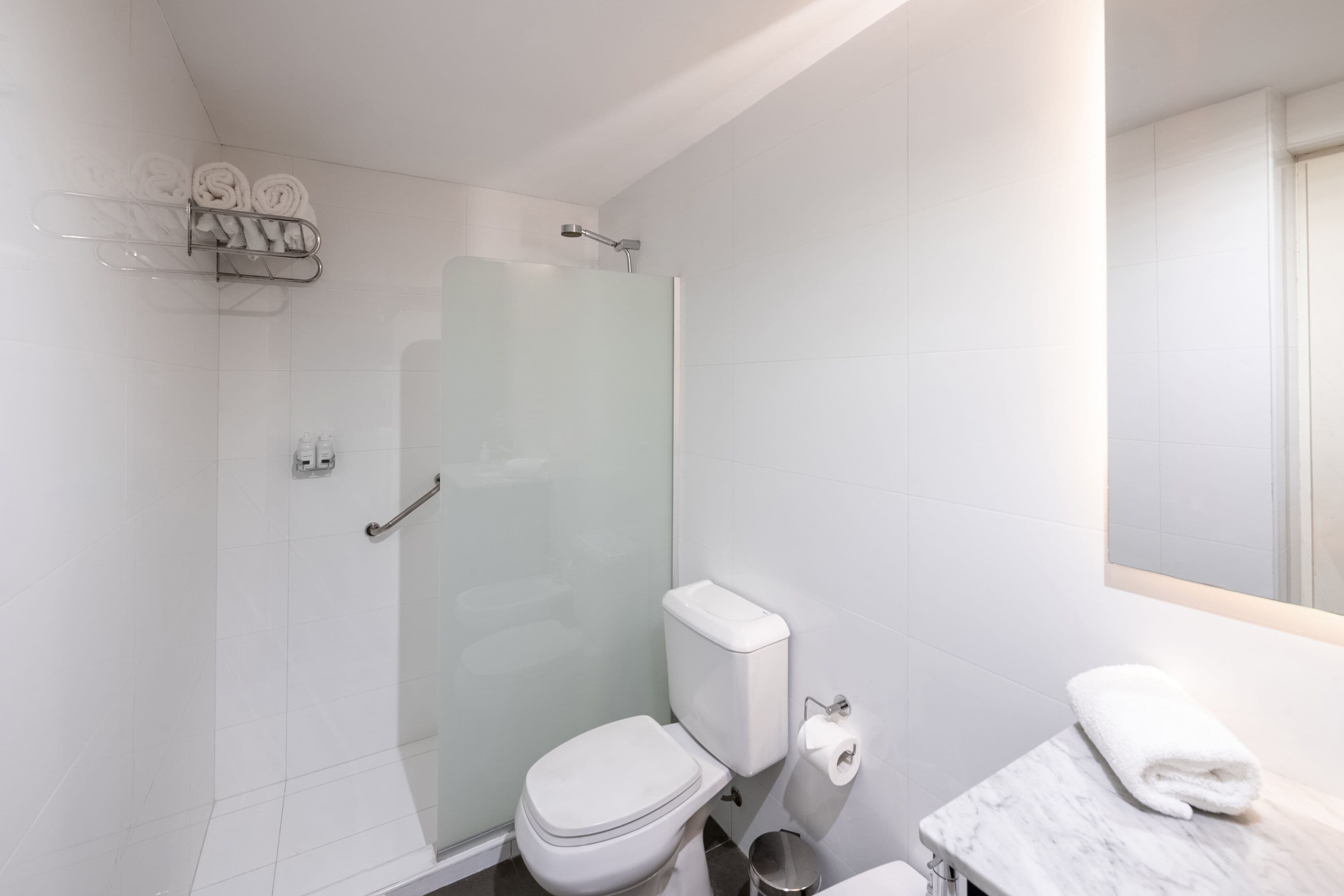 A modern bathroom with a glass shower enclosure, a toilet, and a marble sink with a towel.