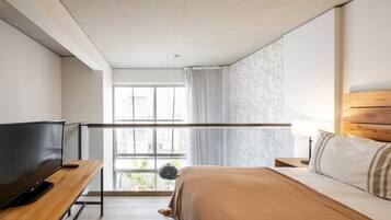 A bedroom with a bed, a TV, a window with curtains, and a view of the outside.