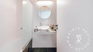 Un baño moderno con cabina de ducha de vidrio, un espejo redondo y encimera de mármol con lavamanos.