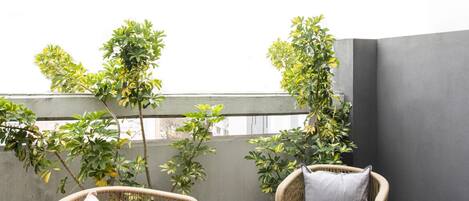 A balcony with two wicker chairs and a small round table, surrounded by potted plants.