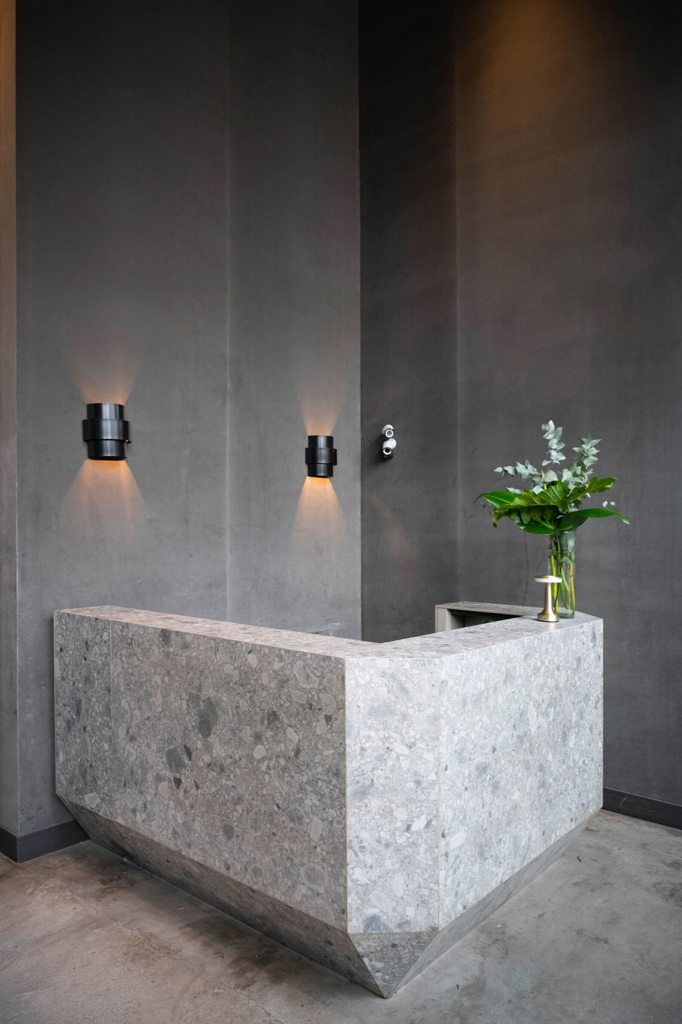 A reception desk with a marble top, two wall-mounted lights, and a vase with a plant.