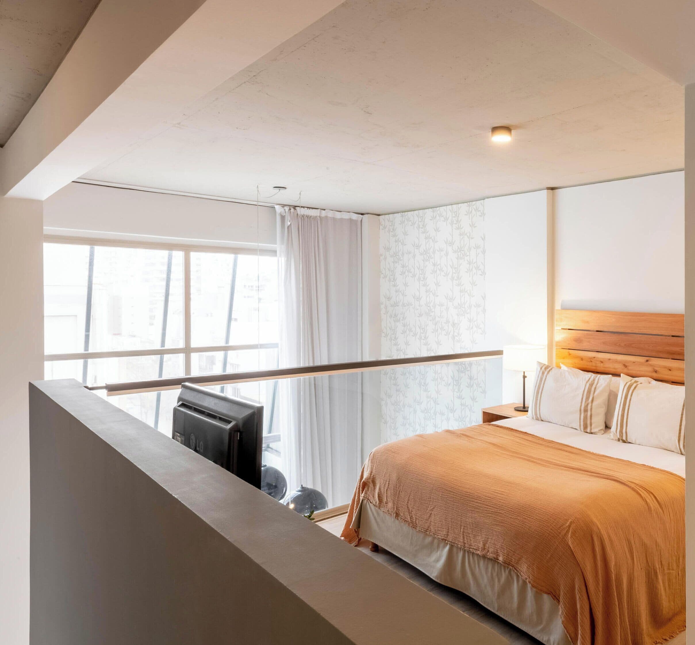 Ein Schlafzimmer mit Bett, Fenster, Vorhang und Blick auf Gebäude.