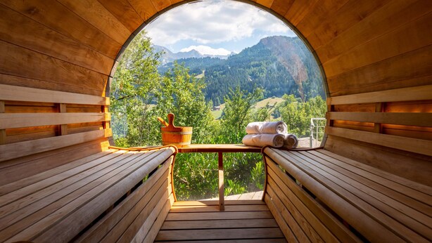 Una sauna de madera con bancos y vistas a un paisaje montañoso a través de un amplio ventanal arqueado.