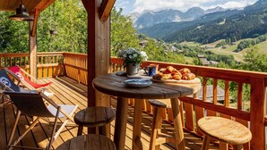 Una terraza de madera con una mesa dispuesta para el desayuno, con vistas a un paisaje montañoso.
