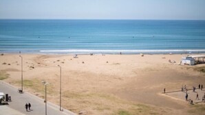Une plage avec un ciel dégagé, un rivage sablonneux et quelques personnes.