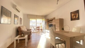 Un salon moderne avec un canapé, une petite table et un coin repas comprenant une table et des chaises. Des œuvres d’art ornent les murs, et une statue de Bouddha est également présente.