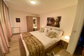 Ein Schlafzimmer mit einem großen Bett, einem Holzschrank, einem Nachttisch mit Lampe sowie einem an der Wand hängenden Bild.