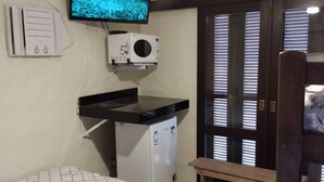 A bedroom with a bed, a desk with a computer, a ceiling fan, a TV, and a window with blinds. - Condomínio Sargento Laranja (Garopaba)