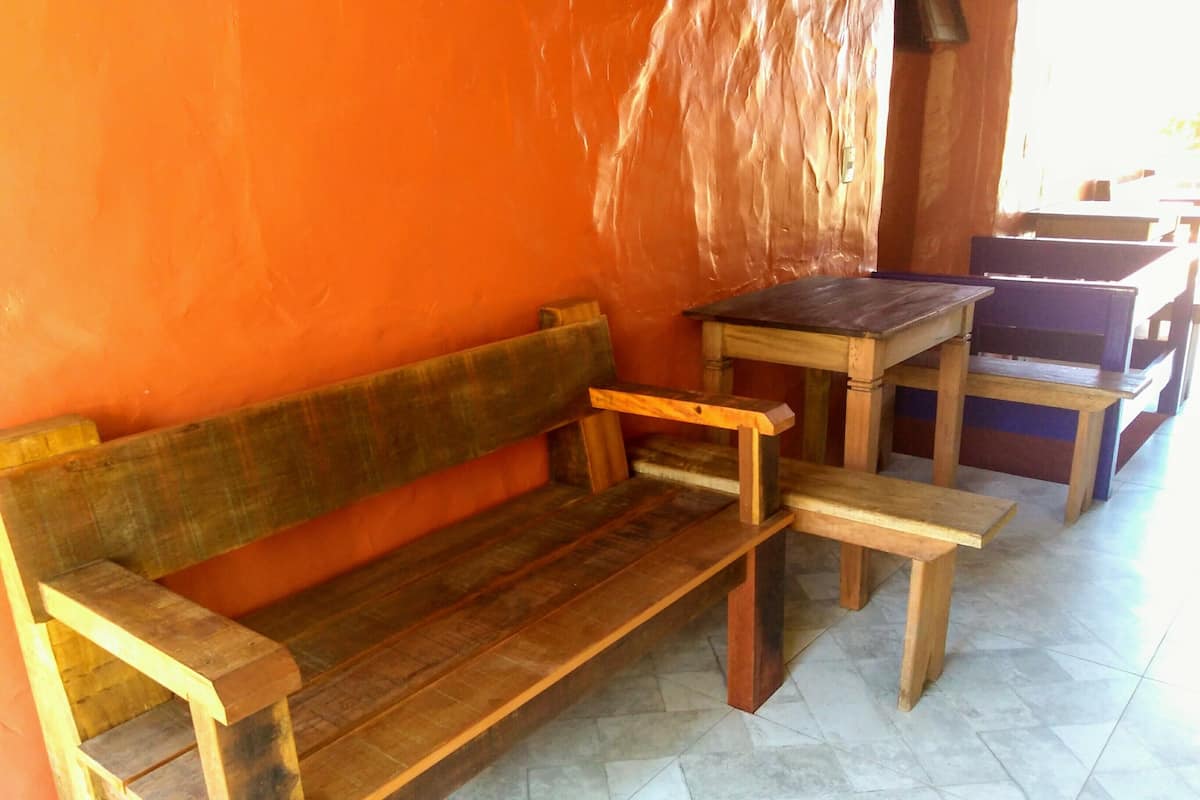 Un banco y una mesa de madera frente a una pared naranja, con suelo de baldosas.
