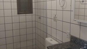 A bathroom with white tiled walls, a white toilet, a granite countertop with a sink, and a mirror above the sink. - Condomínio Sargento Laranja (Garopaba)