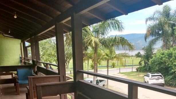 A covered outdoor seating area with wooden benches and a view of a road and greenery. - Condomínio Sargento Laranja (Garopaba)