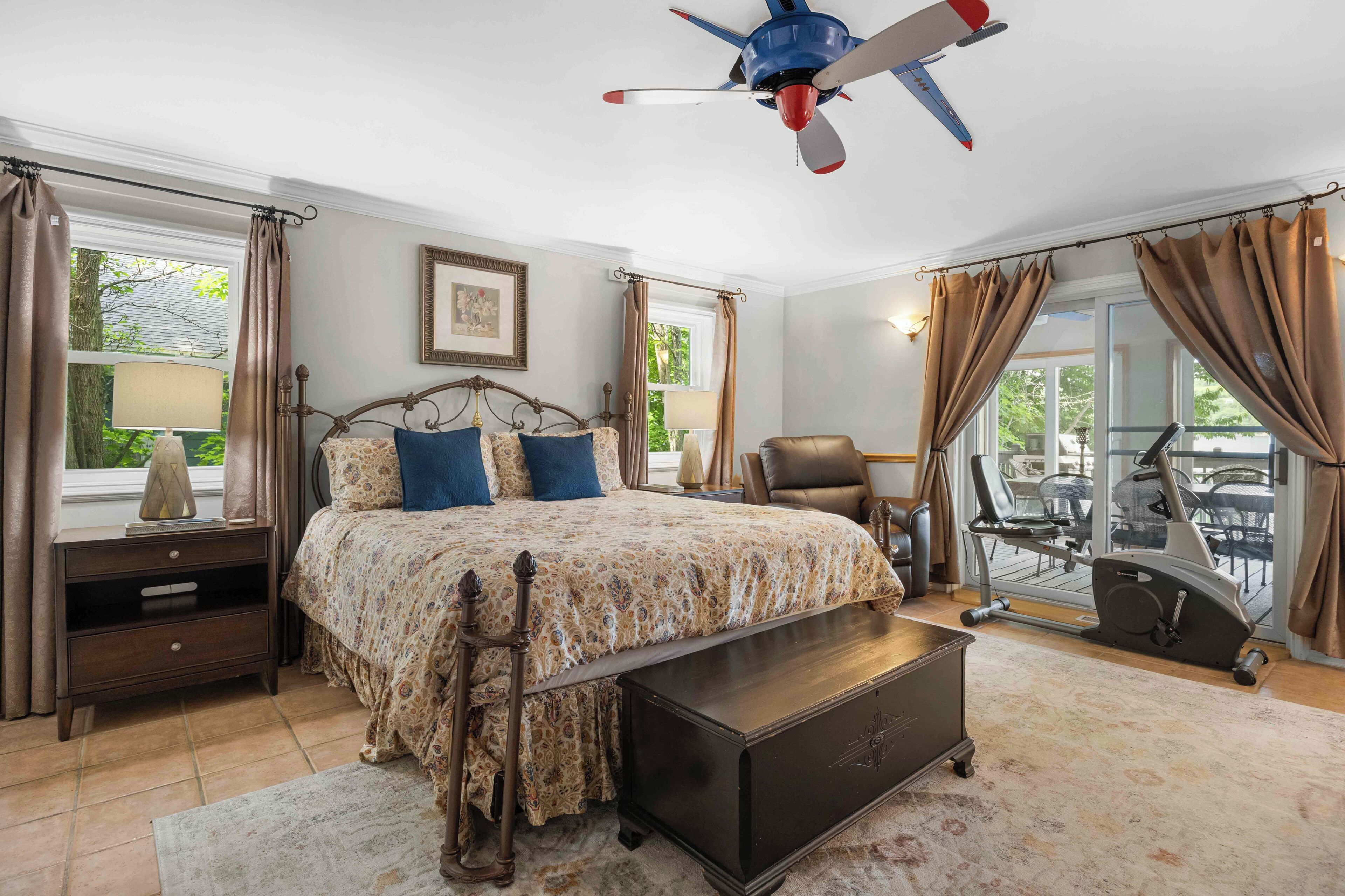 A bedroom with a bed, a desk, a chair, a treadmill, and a ceiling fan.