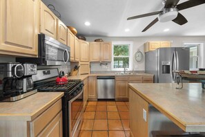 Una cocina con armarios de madera, estufa, microondas, lavavajillas y refrigerador.