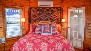 A wooden cabin bedroom with a large bed, two bedside tables with lamps, a patterned headboard, and a door with frosted glass panels.