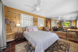 A wooden cabin bedroom with a bed, two bedside tables, a desk, a chair, and a window.