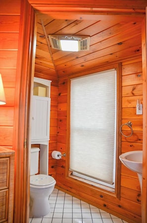 Un baño rústico con cabaña, un inodoro, una ventana con persianas, un lavabo y un armario.