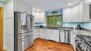 A modern kitchen with stainless steel appliances, white cabinetry, a window with a view, and a blue accent wall. - Maya's Palace: Pet-Friendly Keuka Lake Escape! (Keuka Park)