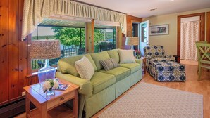A cozy living room with a green sofa, a patterned ottoman, and a wooden coffee table. - Lady of the Lakes Suites 1: Garden View (Branchport)