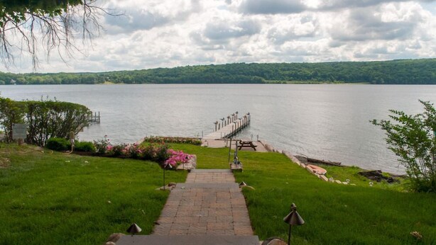 A stone pathway leading to a dock over water, surrounded by greenery and a cloudy sky. - Lady of the Lakes Suites 1: Garden View (Branchport)