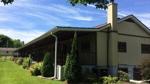 A large, single-story building with a covered porch and a chimney. - Lady of the Lakes Suites 1: Garden View (Branchport)