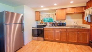 A kitchen with wooden cabinets, stainless steel appliances, and a window with a curtain. - Lady of the Lakes Suites 1: Garden View (Branchport)
