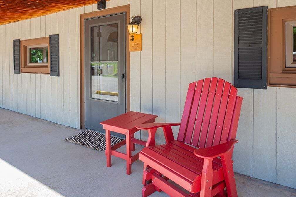 En röd Adirondack-stol och ett litet bord på en betongveranda med ett träbeklätt tak.