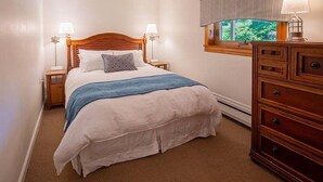 Une chambre à coucher avec un lit en bois, deux lampes de chevet, une commode et une fenêtre donnant sur un paysage verdoyant.