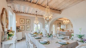 A dining area with a long table set for a meal, white chairs, and hanging crystal chandeliers.