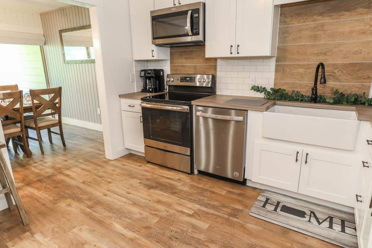 A compact kitchen with white cabinets, stainless steel appliances, and a wooden backsplash.