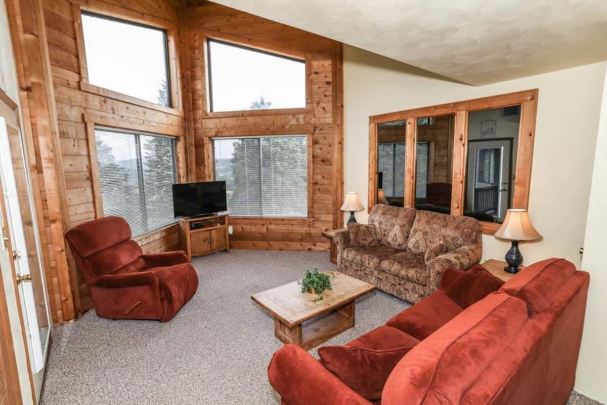 A log cabin interior with a red sofa, a patterned armchair, a wooden coffee table, and a television.