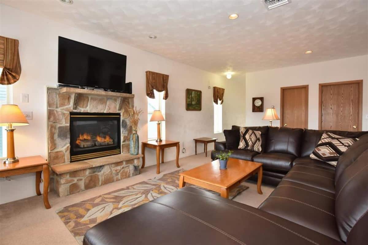 A living room with a stone fireplace, leather sofa, and a flat-screen TV mounted above it.
