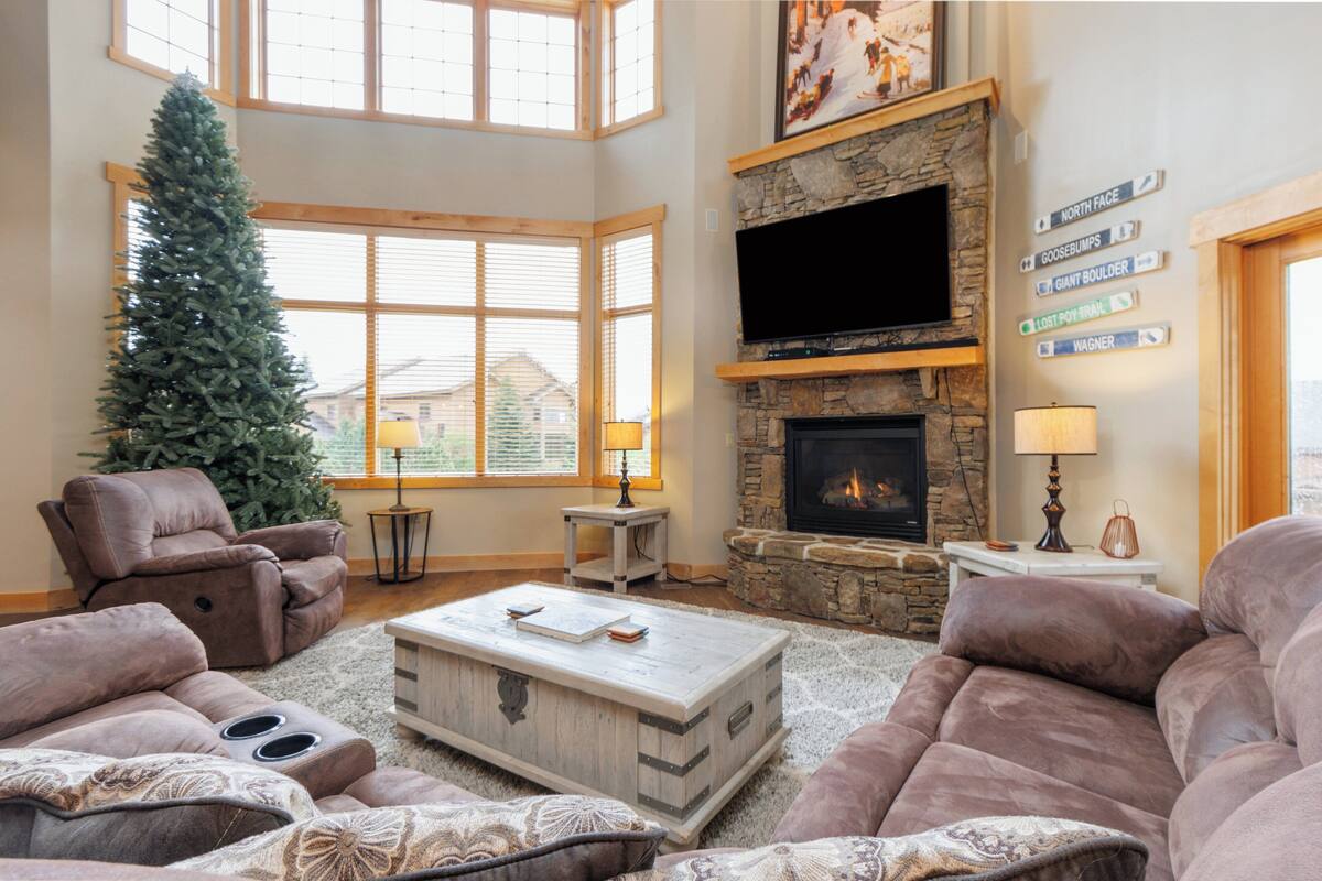 A spacious living room with a stone fireplace, a large TV, and a Christmas tree.