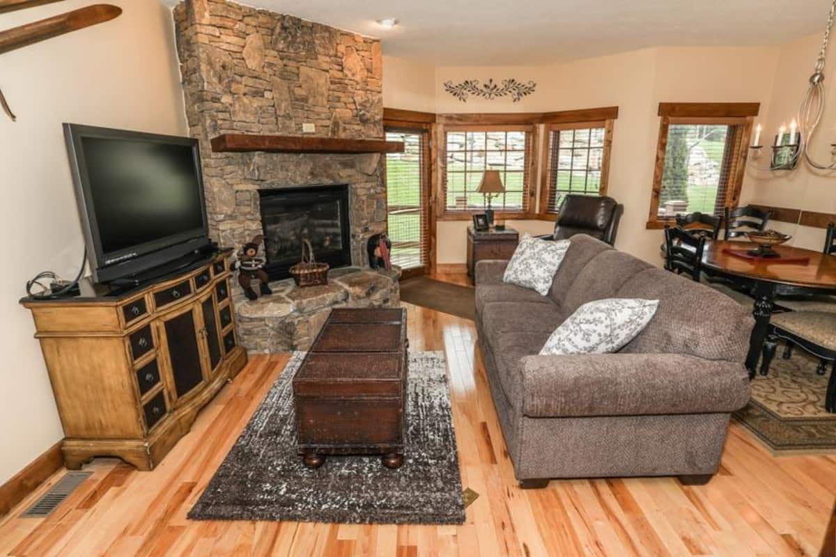 A cozy living room with a stone fireplace, a television, a sofa, and a dining area with a table and chairs.