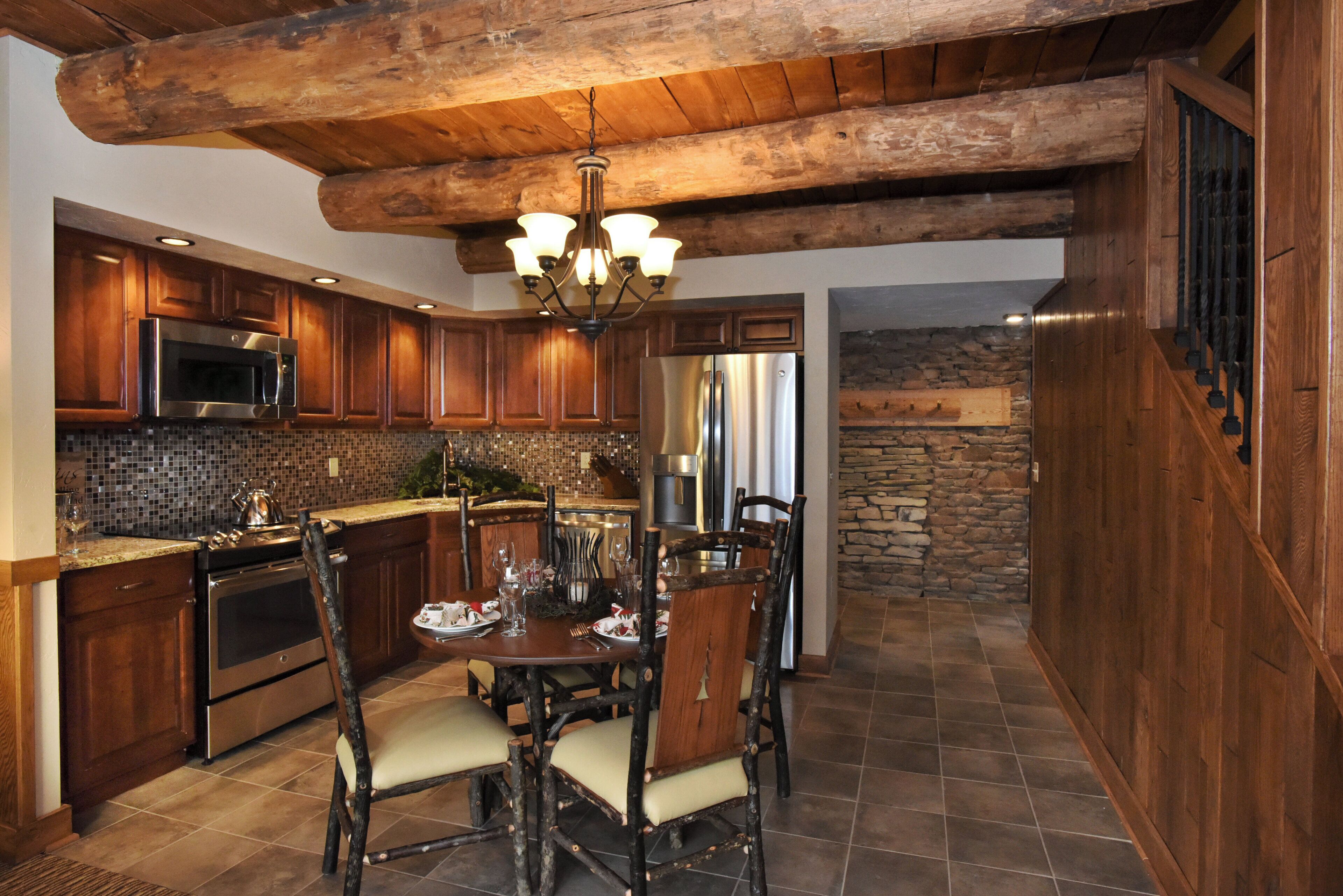 A rustic kitchen with wooden cabinets, a stone wall, and a dining area with a wooden table and chairs.