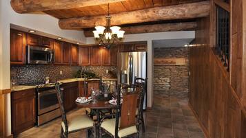A rustic kitchen with wooden cabinets, a stone wall, and a dining area with a wooden table and chairs.