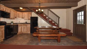 A kitchen with wooden cabinets, a black refrigerator, a wooden dining table set for four, and a staircase leading to a landing.