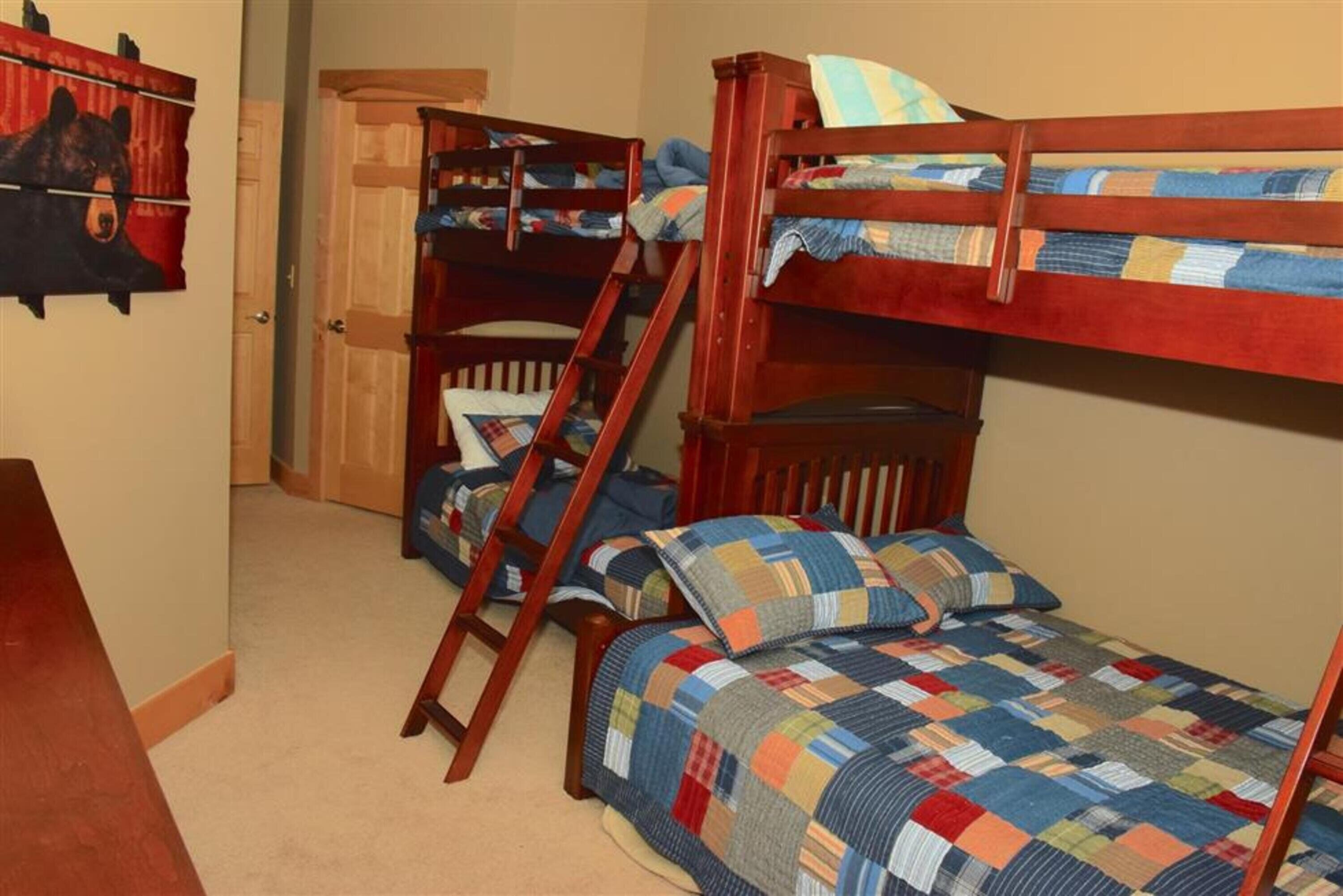 Une chambre avec des lits superposés, une échelle en bois et une couvre-lit matelassé.