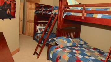 Une chambre avec des lits superposés, une échelle en bois et une couvre-lit matelassé.