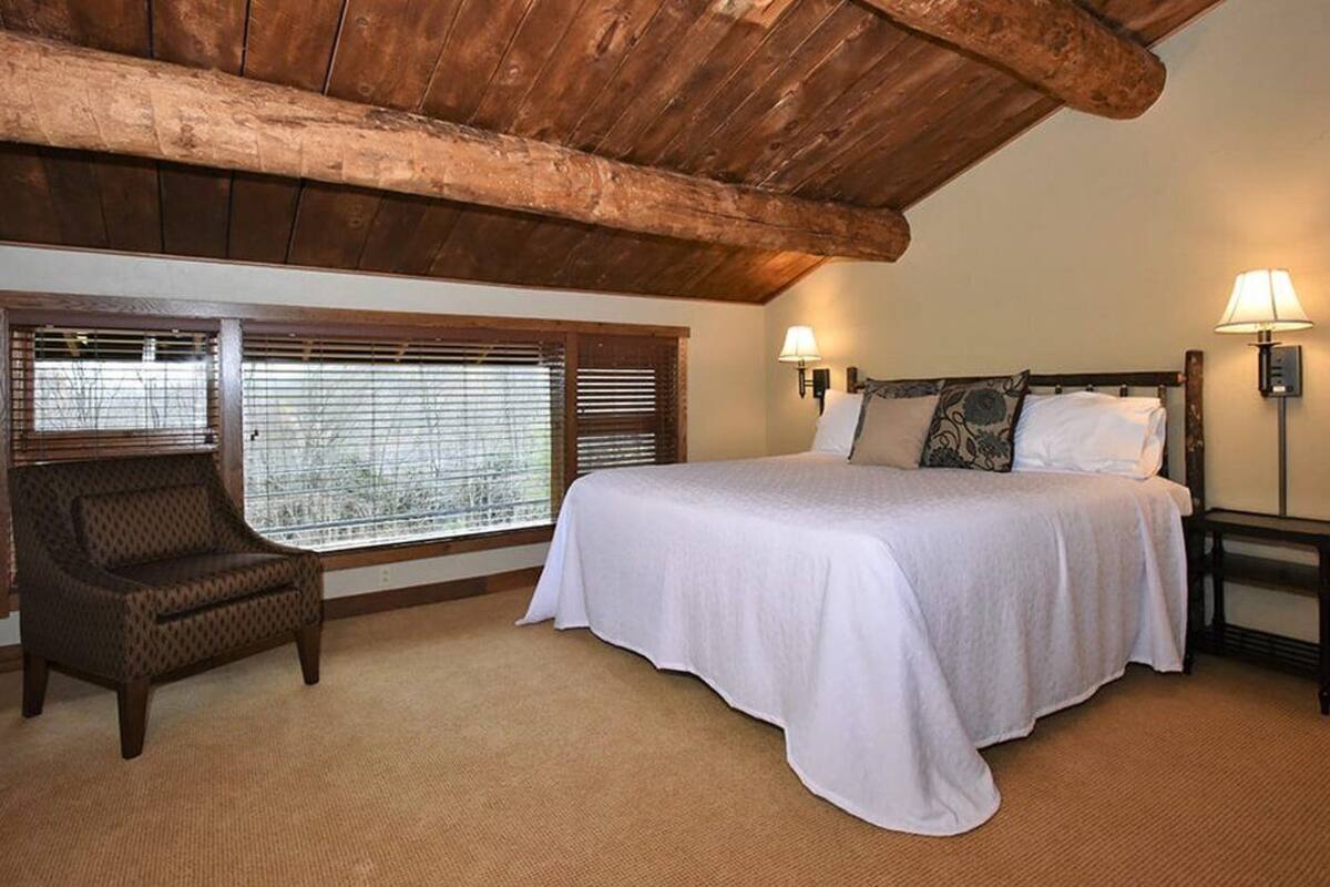 A bedroom with a large bed, two bedside lamps, a chair, and a window with blinds.