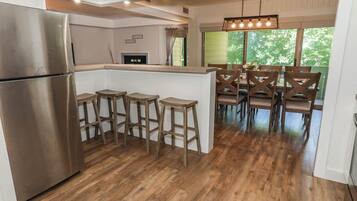 A kitchen with a stainless steel refrigerator, wooden stools, and a dining area with wooden chairs.