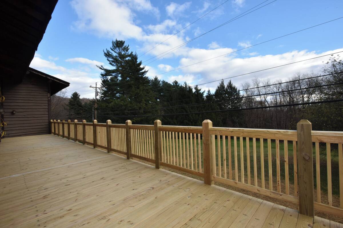 A wooden deck with a railing, a building in the background, and trees.